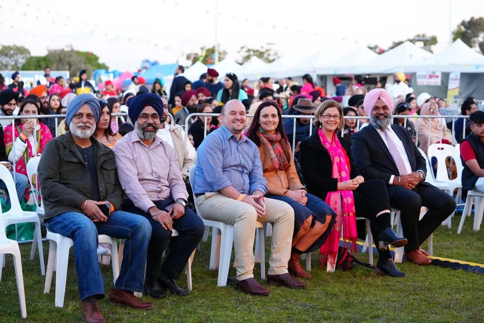 Community elders and invited guests seated in the front row with a large crowd behind them at an outdoor mela