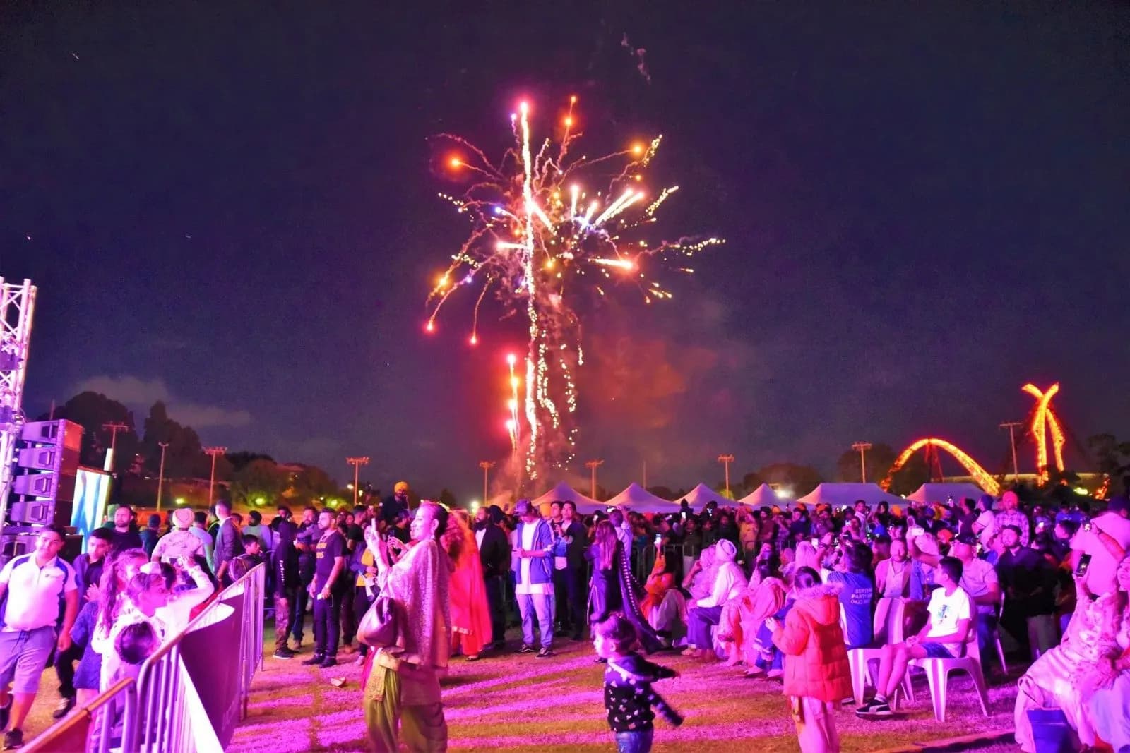 Fireworks burst over a large crowd at an evening WA Punjabi Club mela, with marquees and stage lights in the background